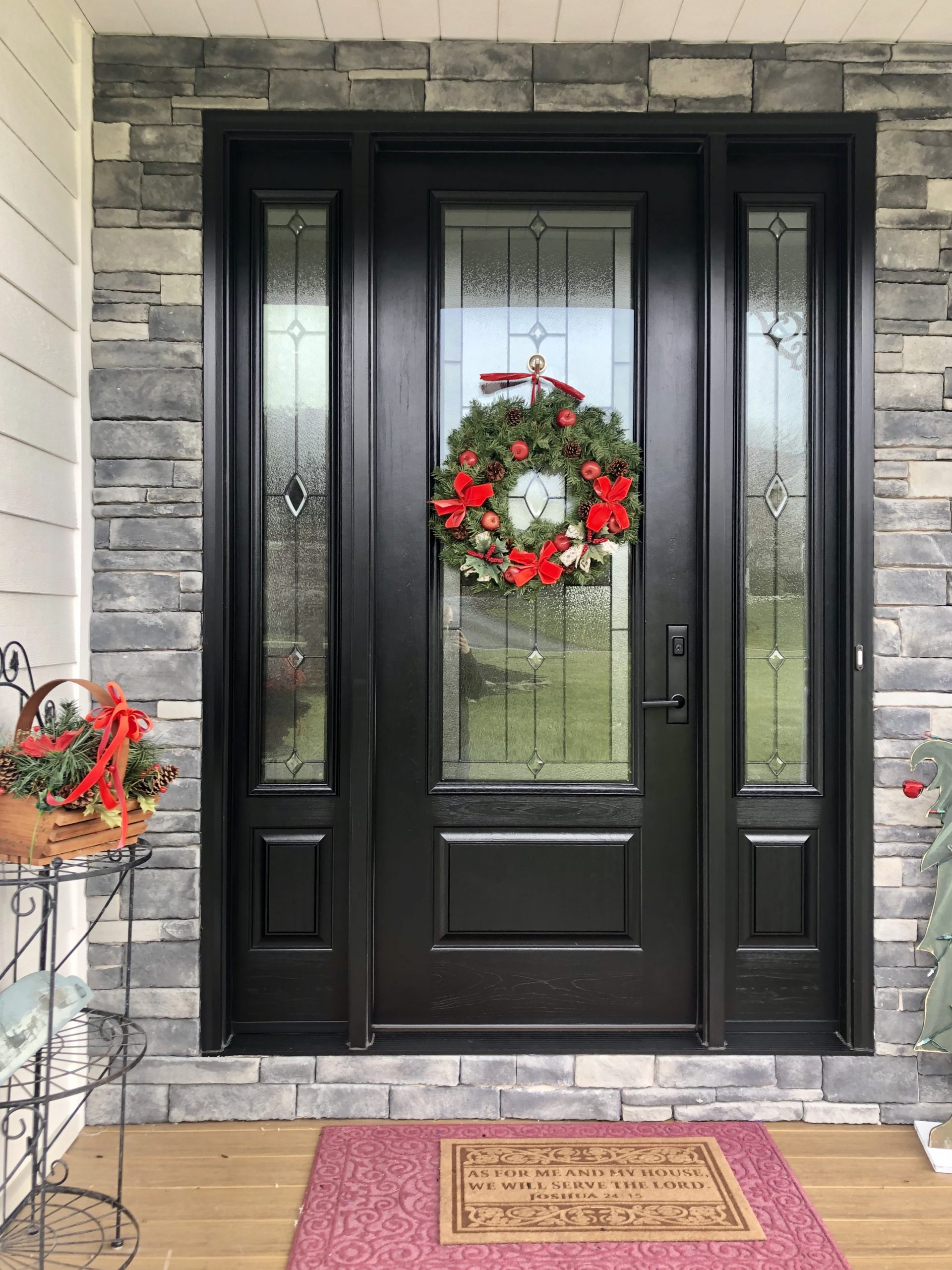 A black front door with windows, with a holiday wreath hanging on it