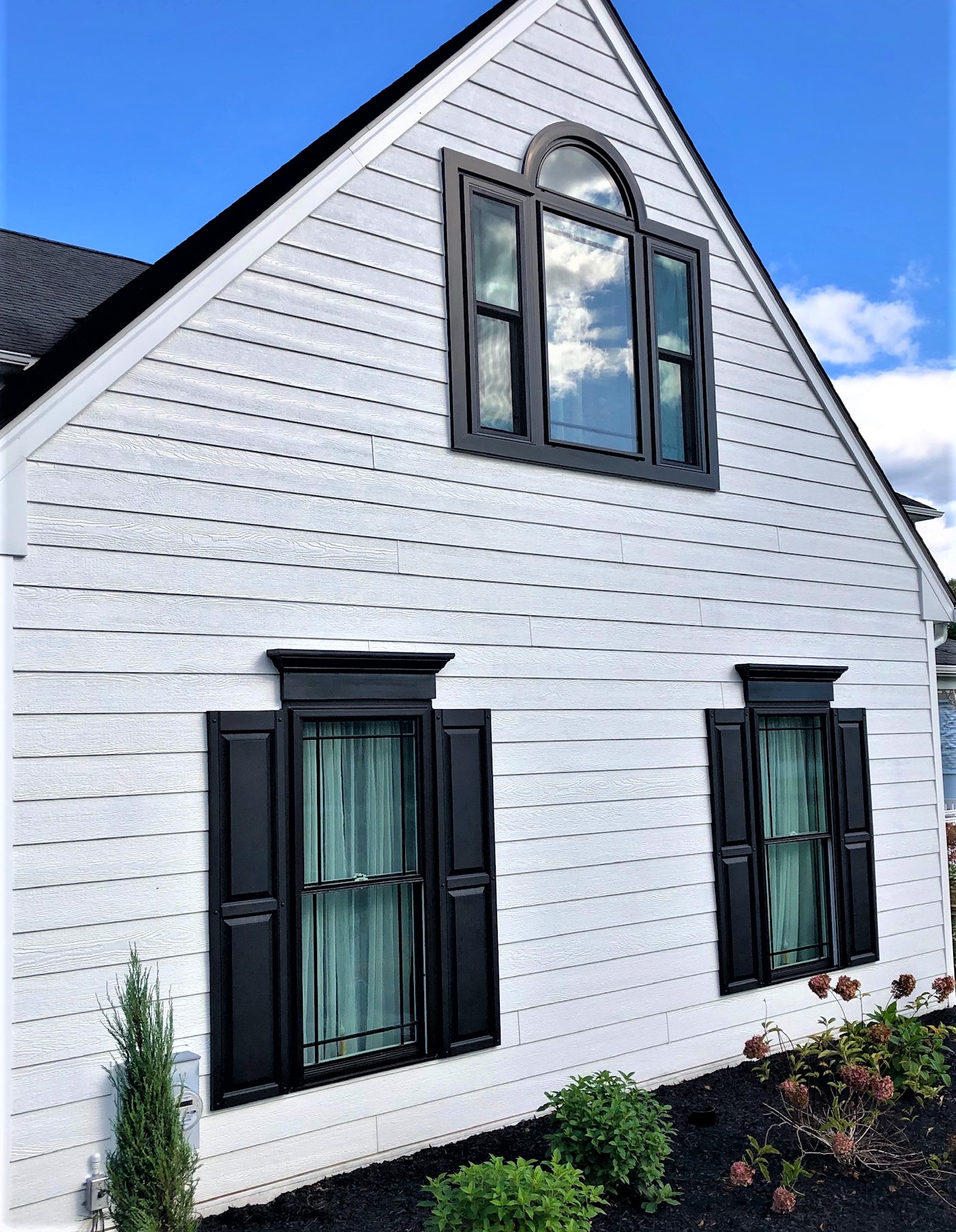 Side view of house with white siding and black windows with black shutters