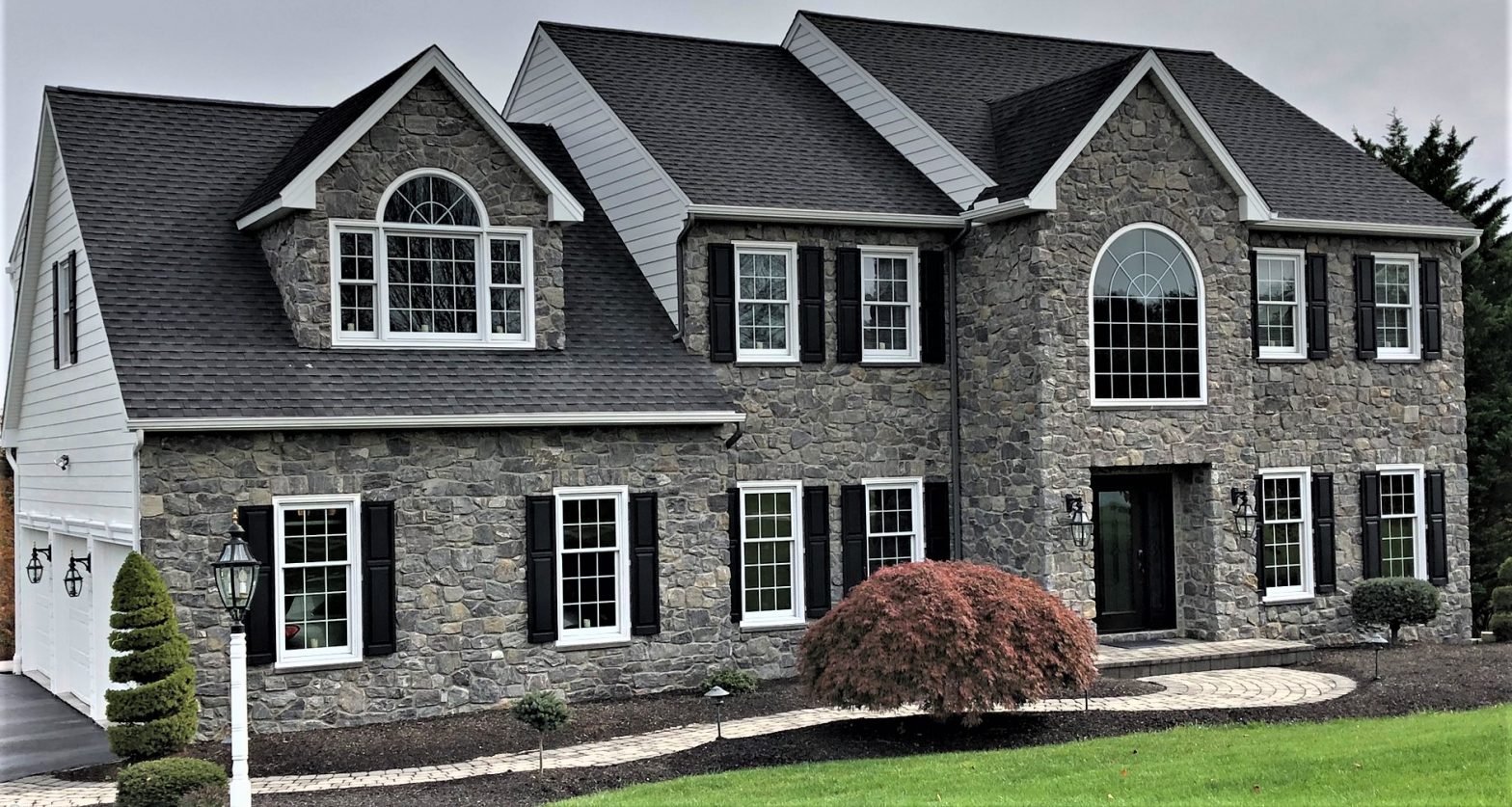 A large home with a stone exterior and white windows with black shutters
