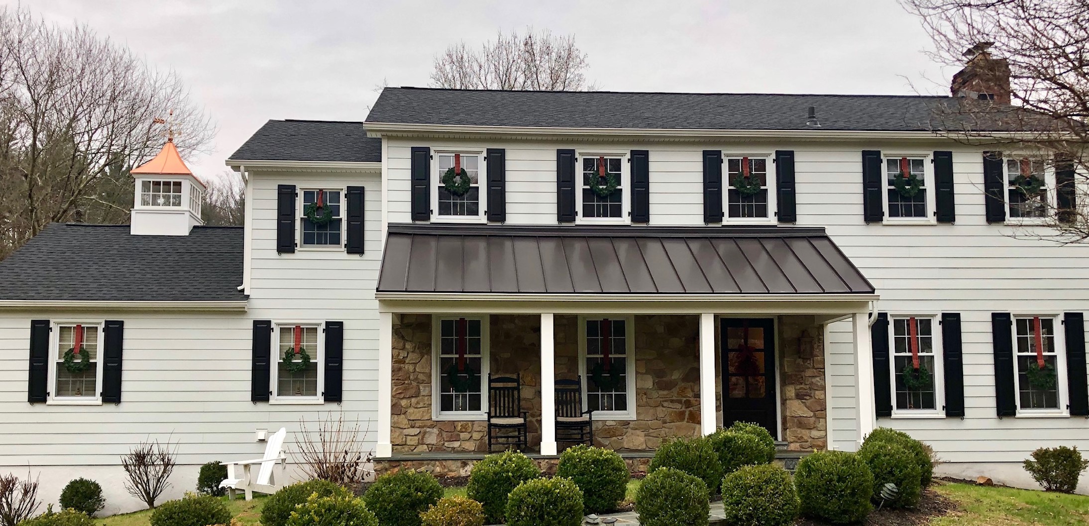 Exterior of a home with white siding, and windows with holiday wreaths hanging
