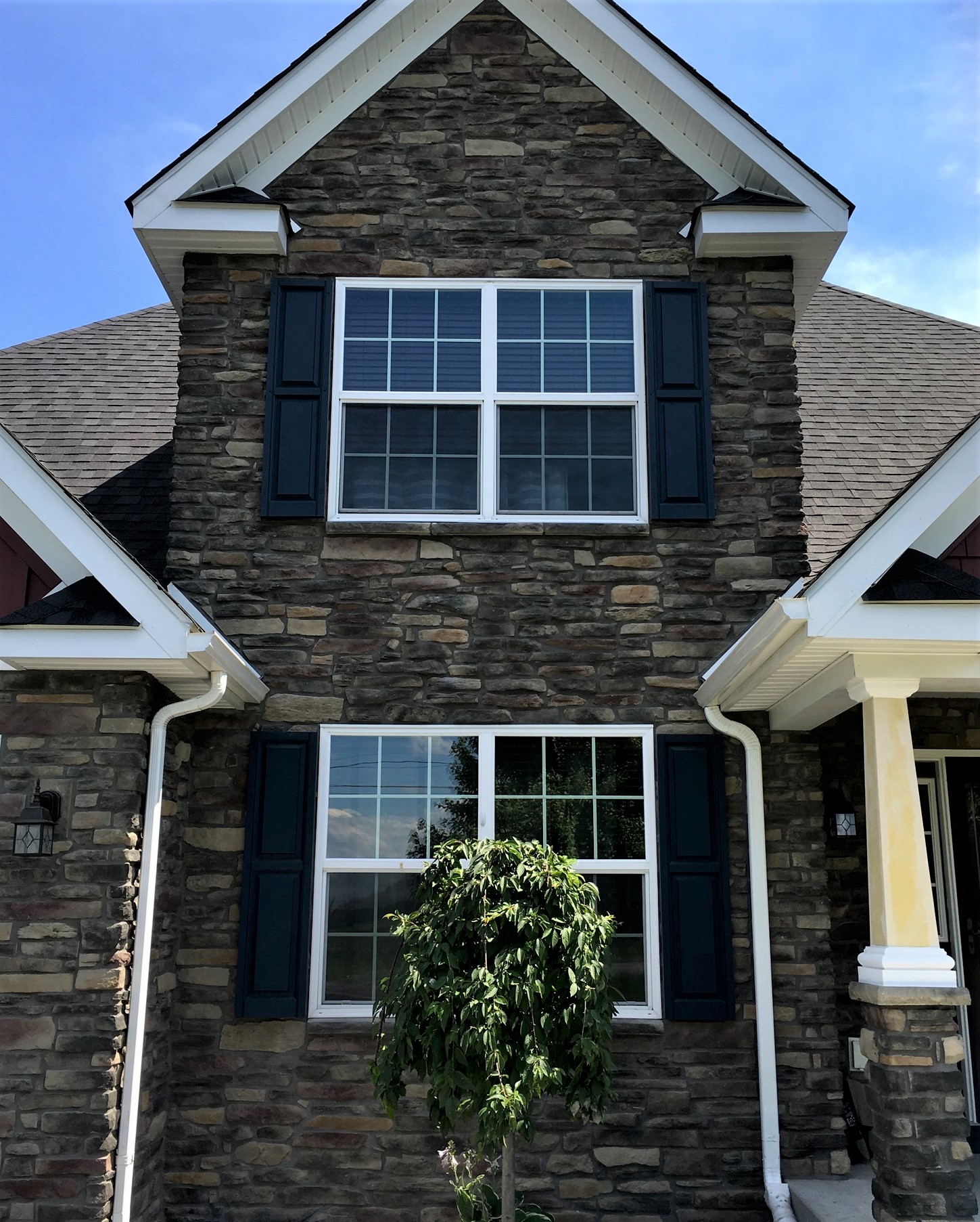 The stone exterior of a home with white windows with black shutters