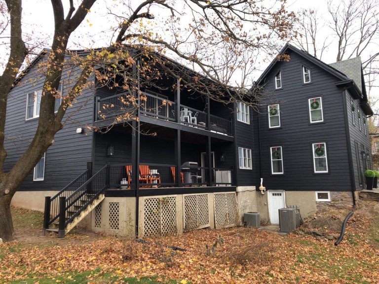 Front left exterior of a large house after LP siding replacement with new onyx black siding, a home addition with black double decks, and new window trim.
