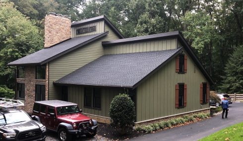 Home exterior after renovation with green LP Diamond Kote siding, new windows with brown shutters, new doors, and a new dark colored roof system in black.