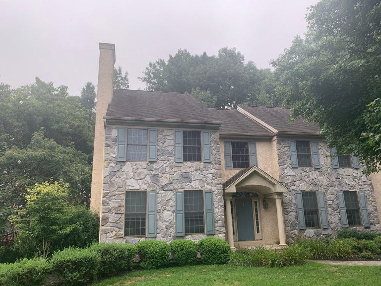 Exterior of large house before installing new off white hardie lap siding with blue window shutters, a dark roof, and gray stone exterior accents.
